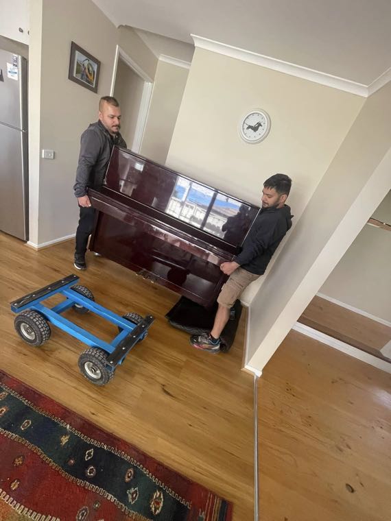 Two Moving Folks removalists carefully carrying an upright piano
